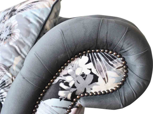 Un vistoso divano a tre posti in stile Chesterfield con delicata decorazione floreale grigia.